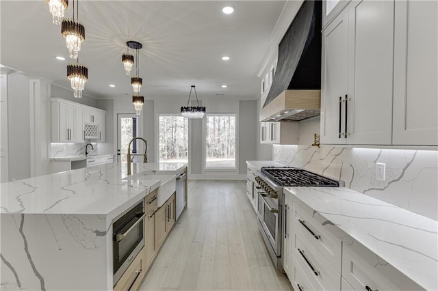 kitchen featuring white cabinets, range with two ovens, hanging light fixtures, a large island, and custom range hood