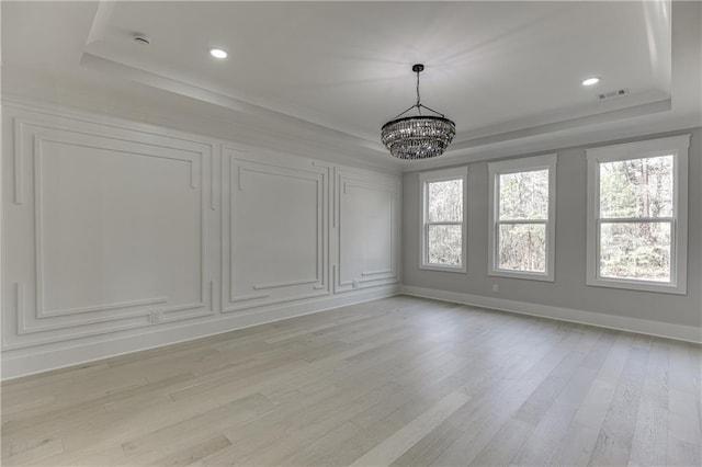 empty room with plenty of natural light, a tray ceiling, light hardwood / wood-style floors, and a notable chandelier