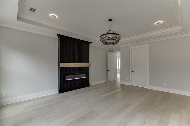 unfurnished living room featuring crown molding, a notable chandelier, a tray ceiling, and light wood-type flooring