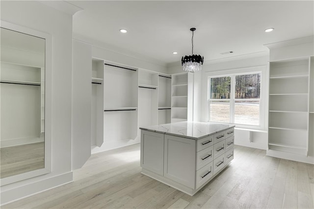 walk in closet featuring a barn door, an inviting chandelier, and light hardwood / wood-style floors