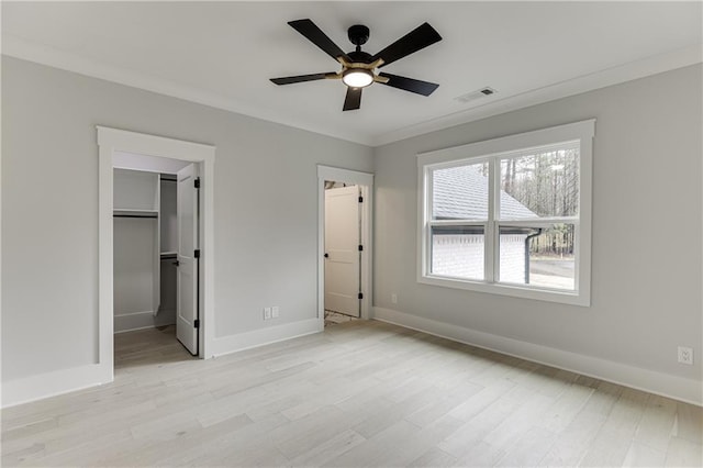 unfurnished bedroom with crown molding, ceiling fan, a spacious closet, a closet, and light wood-type flooring