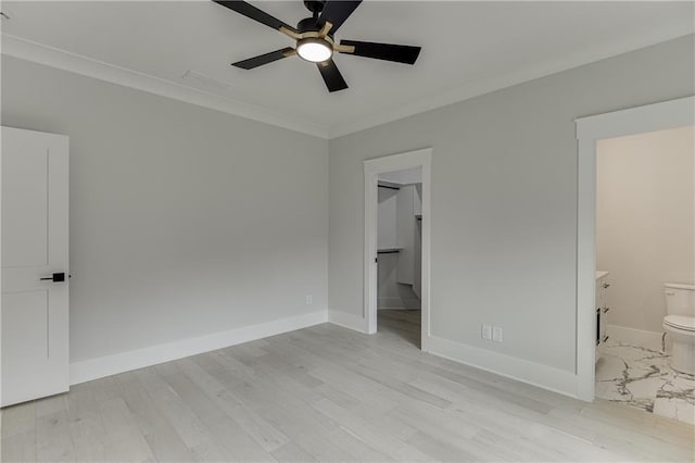 unfurnished bedroom featuring ensuite bath, a walk in closet, ceiling fan, crown molding, and light wood-type flooring