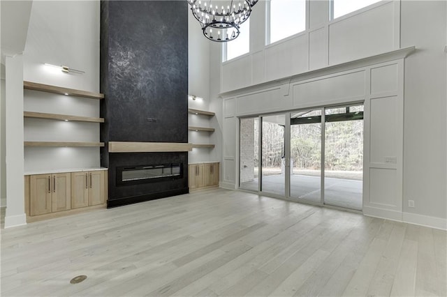 unfurnished living room featuring an inviting chandelier, built in features, light hardwood / wood-style flooring, and a high ceiling