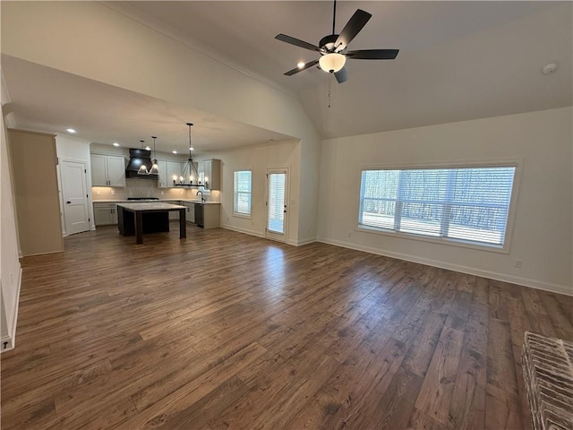 unfurnished living room featuring vaulted ceiling, dark wood-style flooring, ceiling fan with notable chandelier, and baseboards