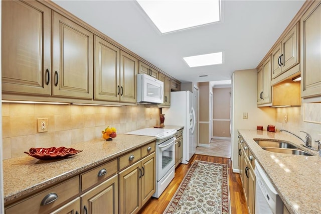 kitchen featuring light hardwood / wood-style flooring, sink, light stone counters, white appliances, and a skylight