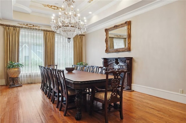 dining area with hardwood / wood-style flooring, a raised ceiling, ornamental molding, and an inviting chandelier