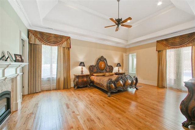 bedroom featuring ceiling fan, light hardwood / wood-style flooring, crown molding, a tray ceiling, and a fireplace