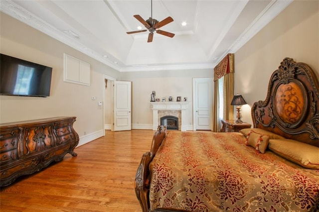 bedroom with light wood-type flooring, a raised ceiling, ceiling fan, and crown molding