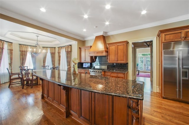 kitchen featuring hardwood / wood-style flooring, high end appliances, premium range hood, and tasteful backsplash