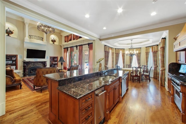 kitchen with sink, light hardwood / wood-style flooring, ornamental molding, an island with sink, and appliances with stainless steel finishes