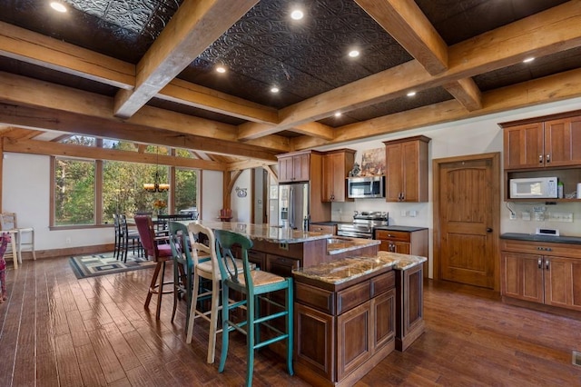 kitchen with a breakfast bar area, beam ceiling, dark wood-type flooring, stainless steel appliances, and a large island