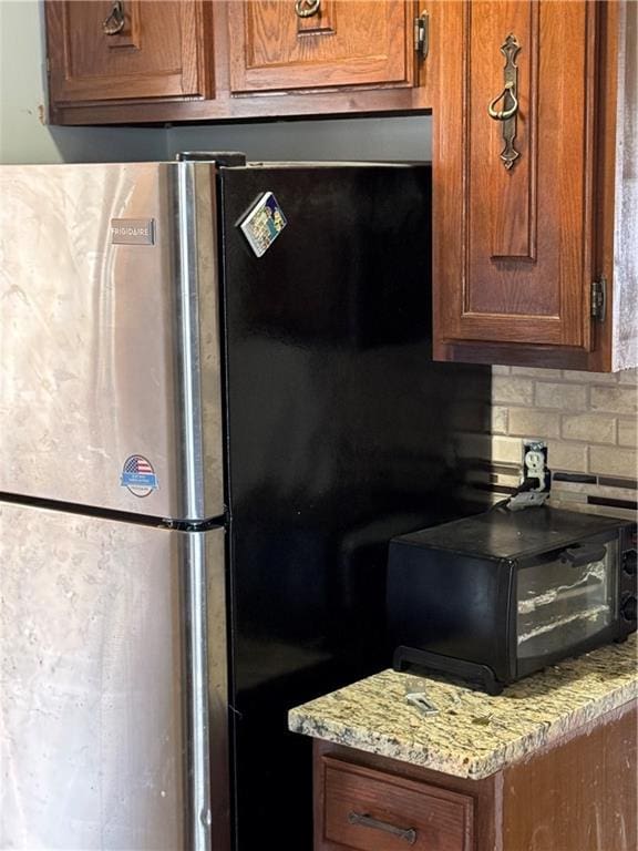 kitchen with light stone countertops, brown cabinetry, a toaster, freestanding refrigerator, and backsplash