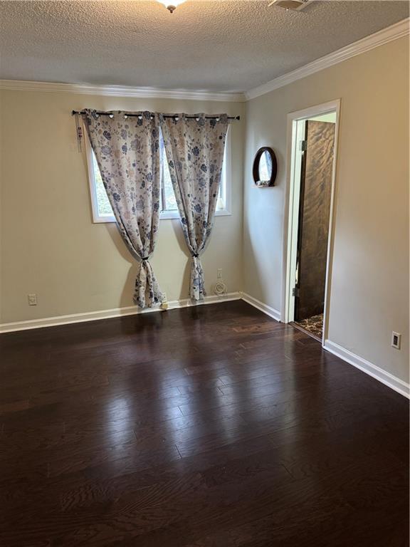 unfurnished room with a textured ceiling, crown molding, baseboards, and wood finished floors