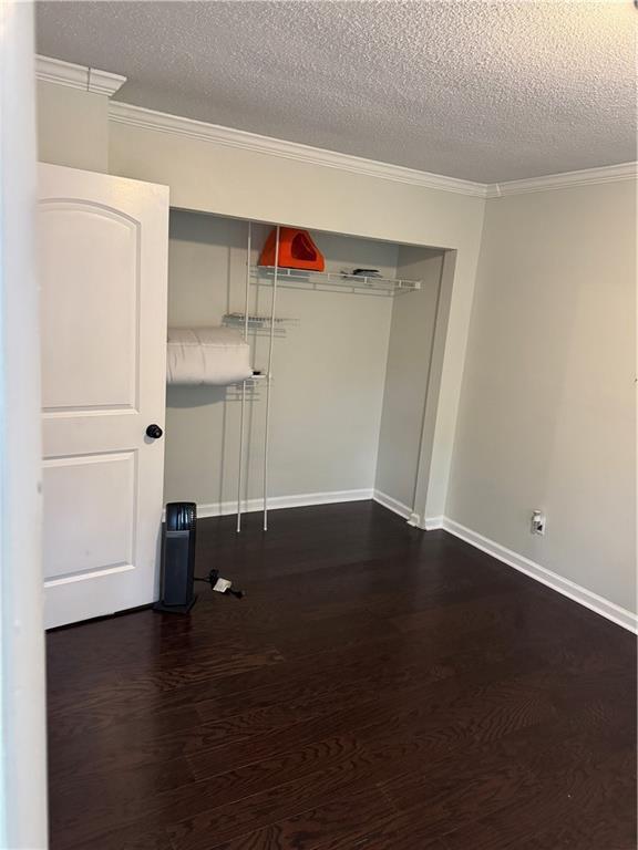 empty room featuring a textured ceiling, dark wood-type flooring, baseboards, and ornamental molding