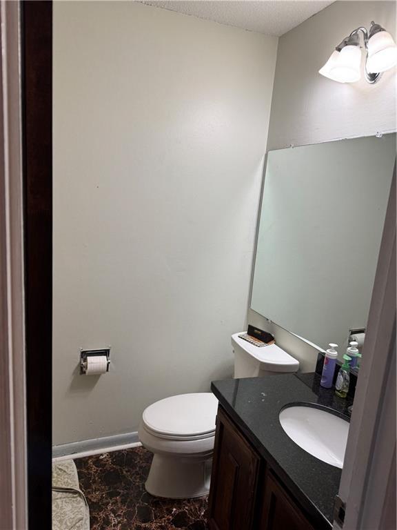 half bathroom with vanity, toilet, baseboards, and a textured ceiling