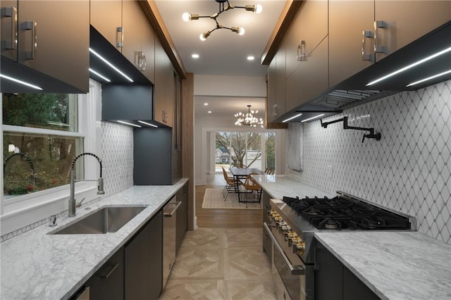 kitchen featuring decorative backsplash, light stone counters, appliances with stainless steel finishes, an inviting chandelier, and a sink