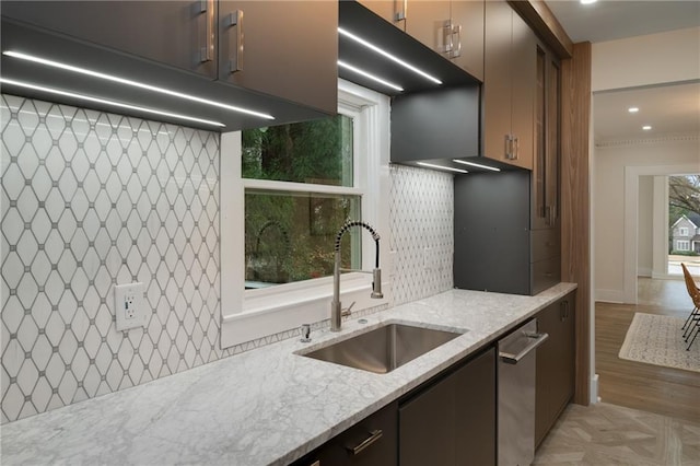 kitchen with light stone counters, light wood-style flooring, a sink, decorative backsplash, and dishwasher