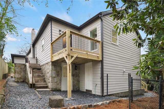 rear view of house featuring stairs, stone siding, a deck, and fence