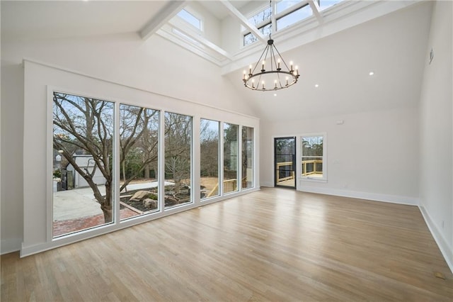 unfurnished living room featuring a chandelier, high vaulted ceiling, baseboards, and wood finished floors