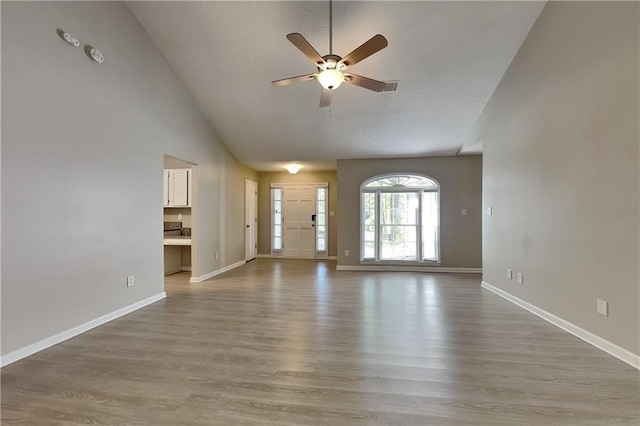 unfurnished living room with hardwood / wood-style floors, ceiling fan, and high vaulted ceiling