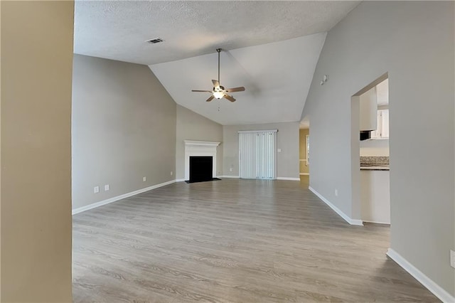 unfurnished living room featuring ceiling fan, light wood-type flooring, a textured ceiling, and vaulted ceiling