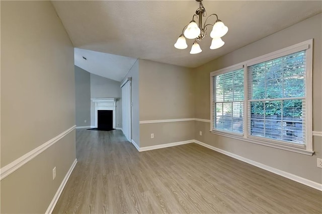 empty room featuring a chandelier, wood-type flooring, and lofted ceiling