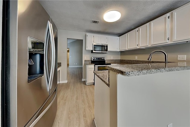 kitchen with white cabinetry, light wood-type flooring, light stone counters, and appliances with stainless steel finishes