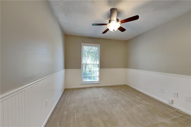 empty room featuring a textured ceiling, light colored carpet, and ceiling fan