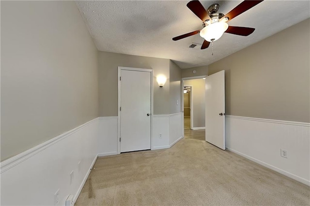 unfurnished bedroom featuring ceiling fan, light carpet, and a textured ceiling