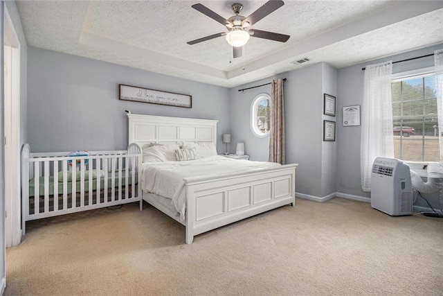 carpeted bedroom with multiple windows, a tray ceiling, a textured ceiling, and ceiling fan