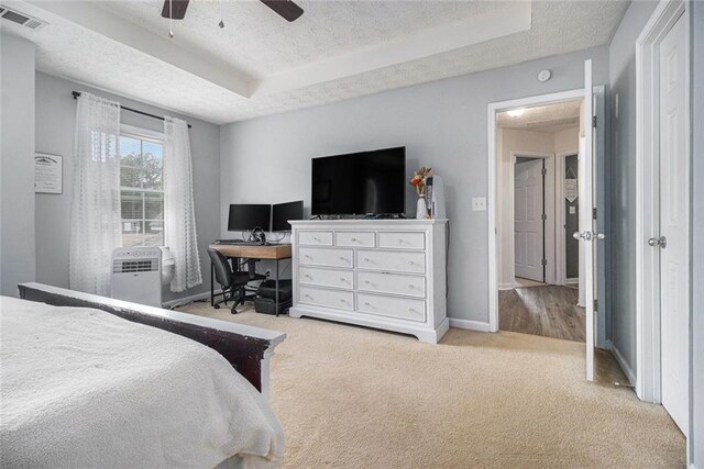 bedroom featuring ceiling fan, a tray ceiling, light carpet, and a textured ceiling