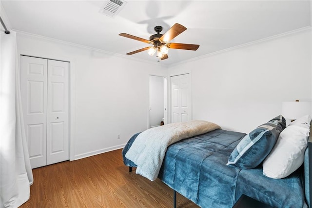 bedroom with multiple closets, hardwood / wood-style floors, ceiling fan, and crown molding