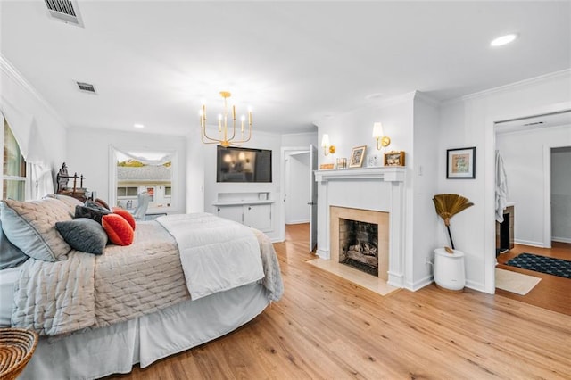 bedroom featuring light wood-type flooring, a chandelier, a tile fireplace, and ornamental molding