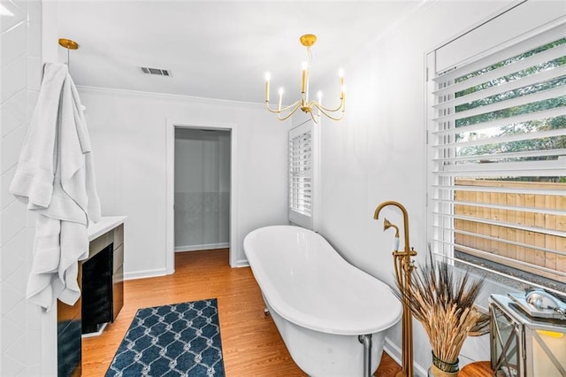 bathroom featuring hardwood / wood-style floors, an inviting chandelier, a tub, and ornamental molding