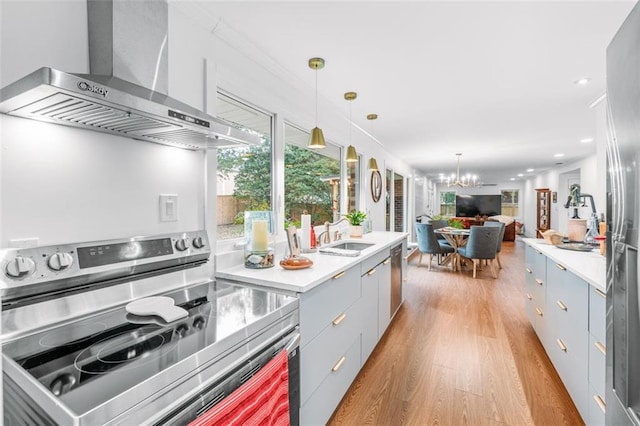 kitchen featuring wall chimney exhaust hood, sink, light wood-type flooring, appliances with stainless steel finishes, and decorative light fixtures