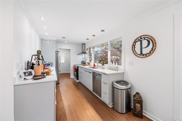 kitchen featuring stainless steel appliances, wall chimney range hood, decorative light fixtures, sink, and light hardwood / wood-style floors