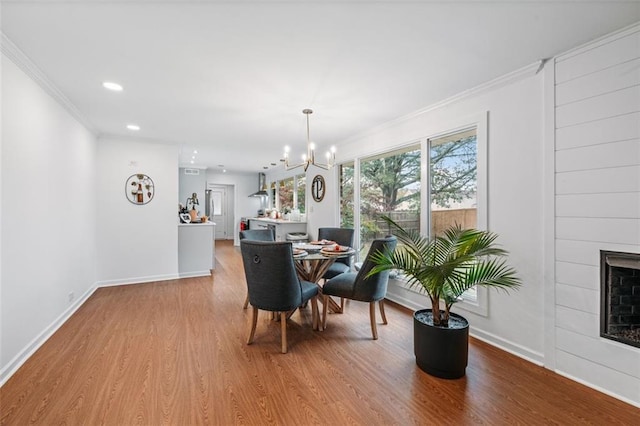 dining space featuring a fireplace, an inviting chandelier, hardwood / wood-style floors, and crown molding