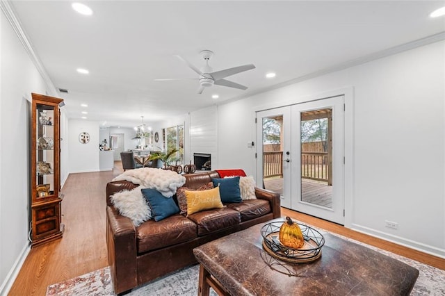 living room featuring french doors, light wood-type flooring, ceiling fan with notable chandelier, and crown molding