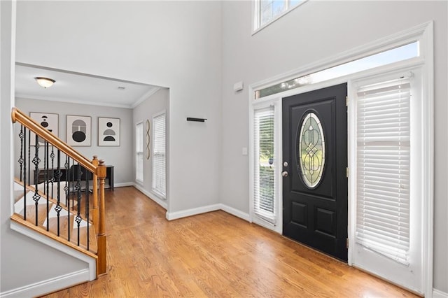 foyer entrance featuring crown molding, stairway, plenty of natural light, light wood-style flooring, and baseboards