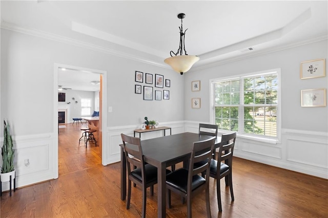 dining room featuring a tray ceiling, wainscoting, a decorative wall, ornamental molding, and wood finished floors