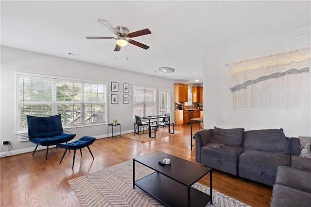 living area featuring ceiling fan, baseboards, and light wood-type flooring
