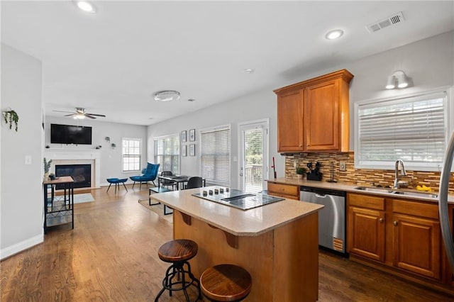 kitchen with stainless steel dishwasher, a sink, a ceiling fan, light countertops, and a glass covered fireplace