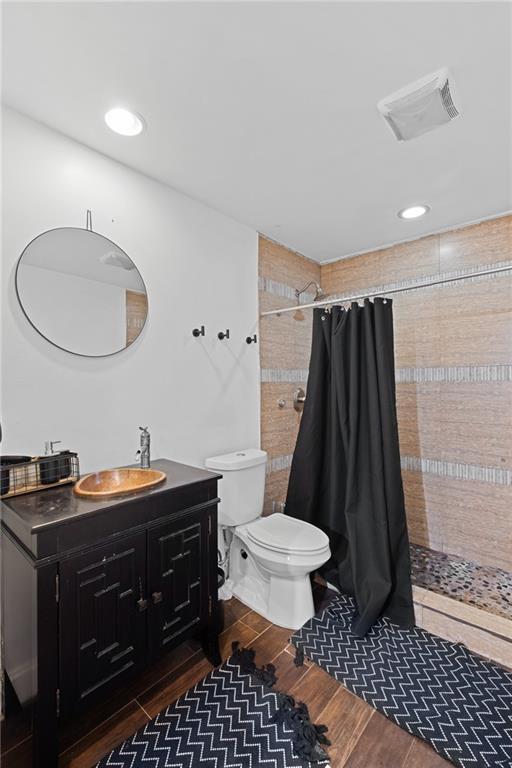 full bathroom with wood finished floors, tiled shower, toilet, vanity, and recessed lighting