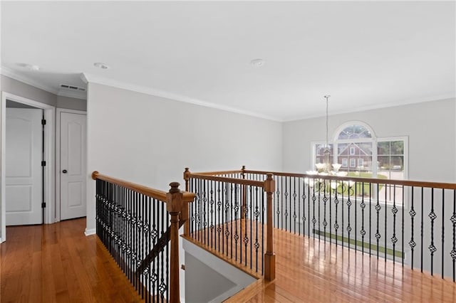 hall with a chandelier, wood finished floors, crown molding, an upstairs landing, and baseboards