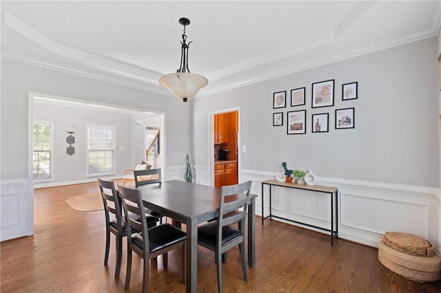 dining room featuring a raised ceiling, wainscoting, wood finished floors, ornamental molding, and a decorative wall