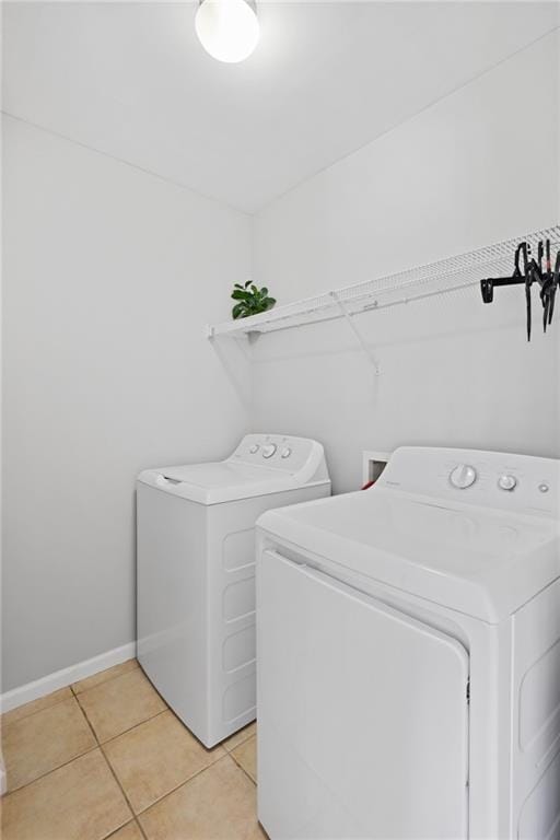 clothes washing area with washing machine and dryer, light tile patterned floors, and baseboards
