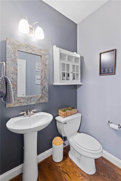 half bath featuring wood finished floors, toilet, and baseboards