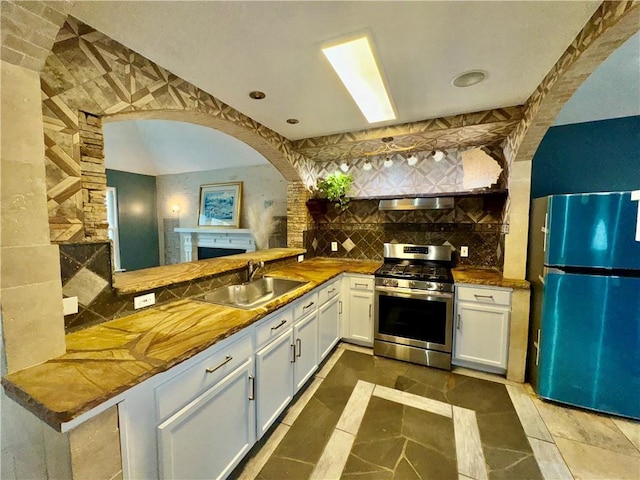 kitchen featuring refrigerator, backsplash, stainless steel range with gas stovetop, a sink, and white cabinetry