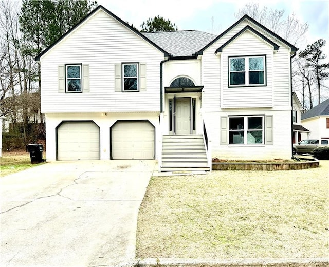 raised ranch featuring a garage, driveway, roof with shingles, and a front yard