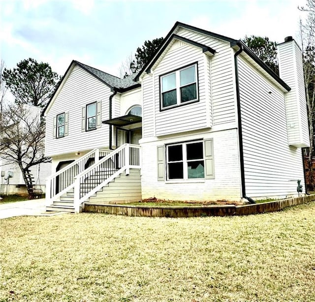 raised ranch with a chimney, brick siding, stairway, and a front lawn